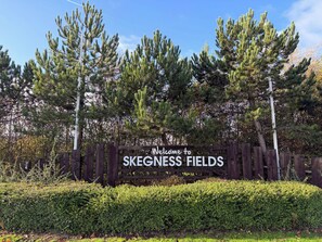 A wooden sign with 'Welcome to Skeenness Fields' written on it, surrounded by greenery and trees. - Palm Grove 2 - UKC9557 (Chapel St Leonards)