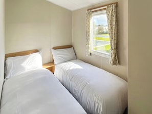 Ein Zimmer mit zwei Einzelbetten, einem Vorhangfenster und Blick auf eine grüne Landschaft.