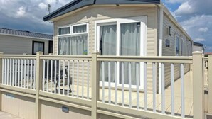 Une maison mobile dotée d’une terrasse clôturée, de grandes fenêtres et d’un toit plat.
