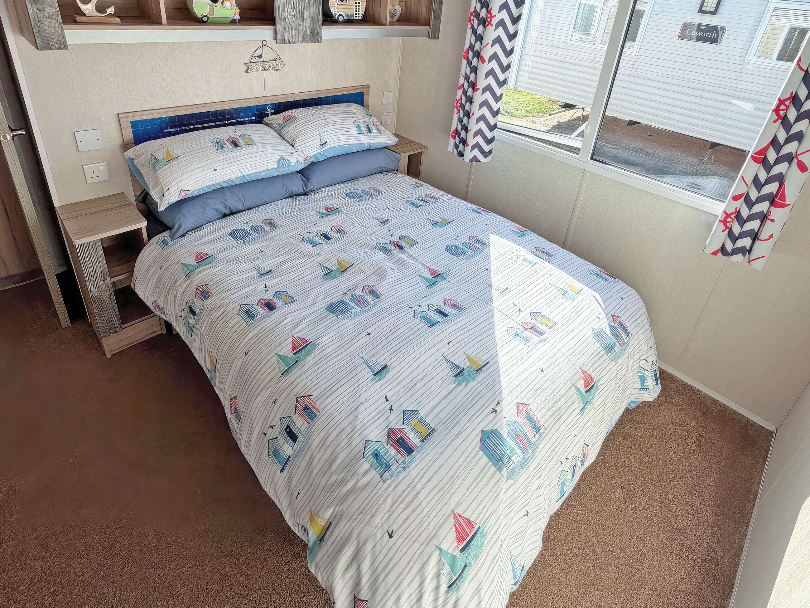 A bedroom with a bed, a nightstand, a window with curtains, and a view of a house outside.