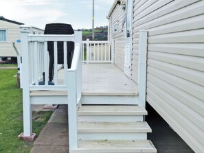 Eine weiße Holztreppe führt zu einem Deck mit weißer Geländer und einem schwarzen Gegenstand auf der linken Seite.