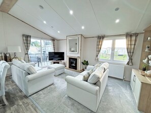 Ein modernes Wohnzimmer mit Kamin, weißen Sofas, einem Flachbildfernseher und großen Fenstern.