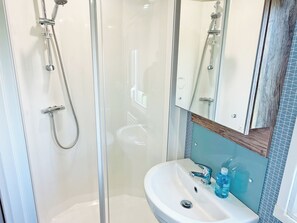 Ein Badezimmer mit einer Duschkabine, einem weißen Waschbecken mit Chromarmatur und einem Spiegel über dem Waschbecken.