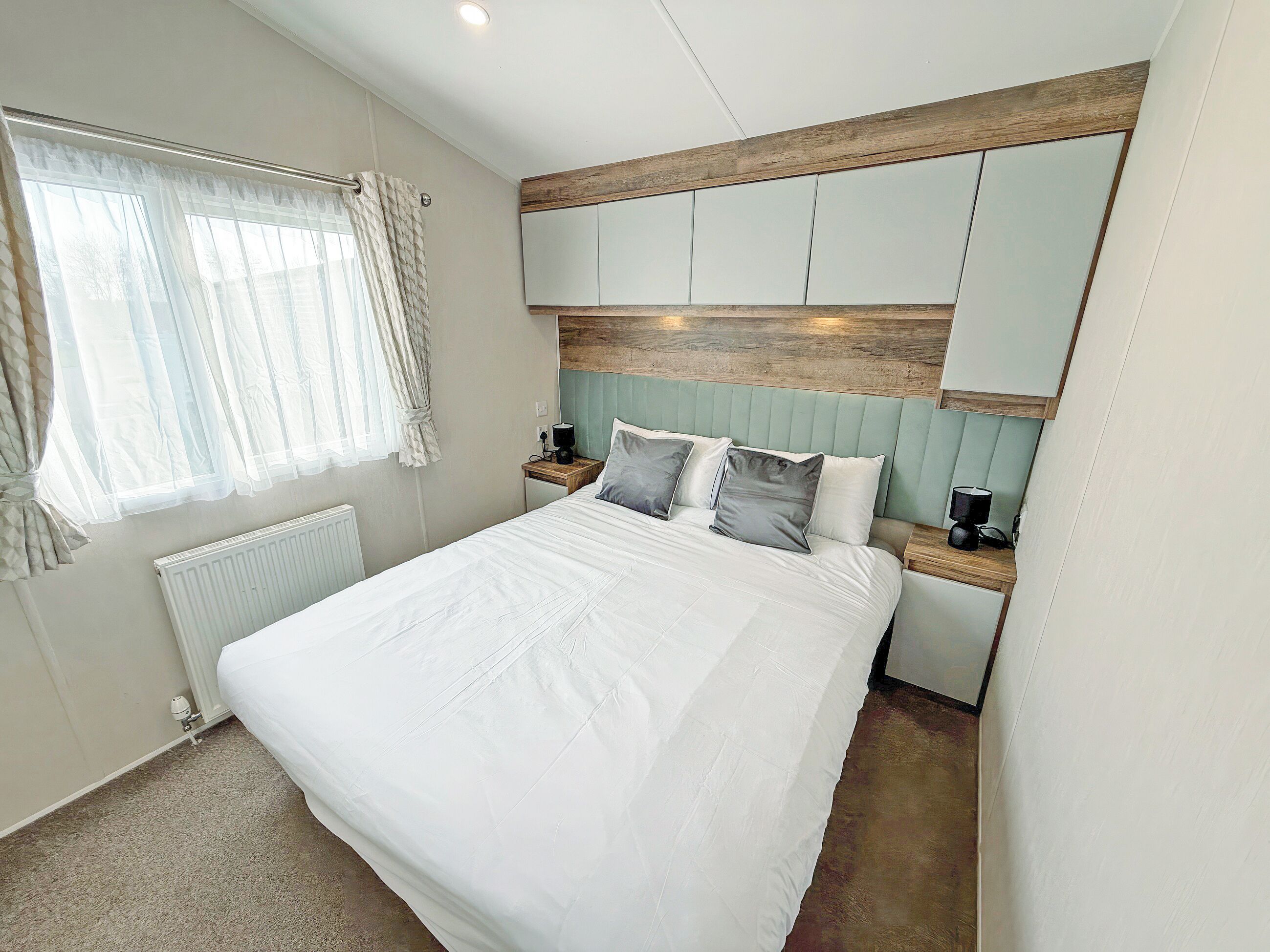 A bedroom with a bed, a nightstand, a lamp, a radiator, and a window with curtains.