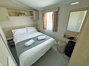 Ein Hotelzimmer mit Bett, einem kleinen Regal mit Pflanzen, einem Fenster mit Vorhängen, einem Spiegel und einem Mülleimer.