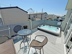 Eine Dachterrasse mit Whirlpool, zwei Korbstühlen, einem kleinen Tisch und einem gemusterten Teppich.