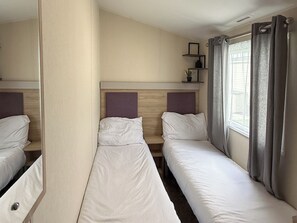Ein Hotelzimmer mit zwei Einzelbetten, einer Kopfteil, einer kleinen Ablage mit Pflanze und einem Fenster mit Vorhängen.