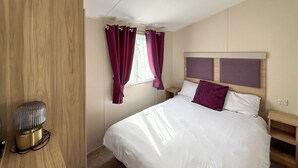 Un dormitorio con cama, cortinas, mesita de noche y lámpara.