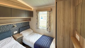 Quarto com duas camas, janela com cortinas, cabeceira com padrão geométrico e guarda-roupa de madeira.