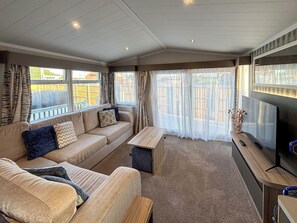 A living room with a sofa, coffee table, TV, and large windows. - Sunnymede A6 - UKC9568 (Ingoldmells)