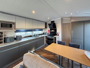 A compact kitchenette with a microwave, toaster, sink, and stove. There is a dining table with chairs and a sofa. - Sunnymede A6 - UKC9568 (Ingoldmells)
