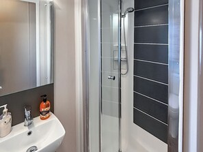 A bathroom with a white sink, a mirror, a shower enclosure, and a dark tiled wall. - Sunnymede A6 - UKC9568 (Ingoldmells)