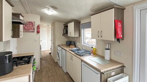 A compact kitchen with a stove, microwave, sink, and a small refrigerator. - Sunnymede D1 - UKC9574 (Ingoldmells)