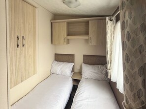 Habitación pequeña con dos camas individuales, armario de madera y una mesita.