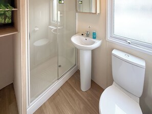 Un baño con ducha envuelta en vidrio, lavamanos pedestal y retrete.