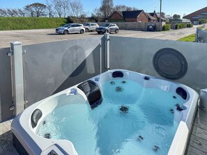 Un jacuzzi con panel de control, rodeado por una valla, con un estacionamiento y casas al fondo.