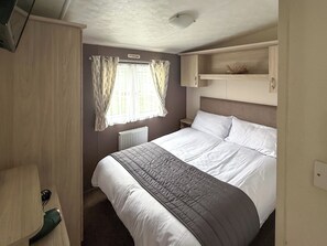Ein Schlafzimmer mit Bett, Kleiderschrank, Heizkörper und einem Fenster mit Vorhängen.