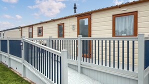 A mobile home with a white exterior, a wooden deck, and a fenced outdoor area. - Sunnymede D1 - UKC9574 (Ingoldmells)