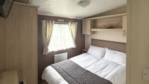 A bedroom with a bed, a wardrobe, a radiator, and a window with curtains. - Sunnymede D1 - UKC9574 (Ingoldmells)
