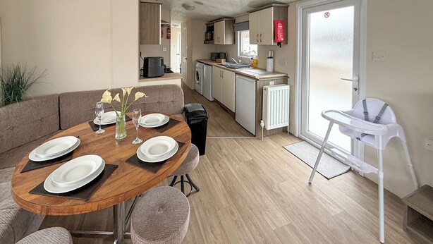 A compact kitchen with a dining area, a white chair, and a radiator. - Sunnymede D1 - UKC9574 (Ingoldmells)