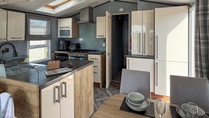 Een compacte keuken met een centraal eiland, een eethoek met een tafel voor twee personen, en een zicht op de aangrenzende woonruimte.