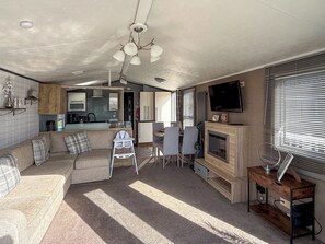 Ein kompakter Wohnbereich mit Sofa, Esstisch, Fernseher, Kamin und Küchenzeile.