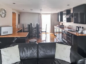 A modern kitchen with black cabinets, a microwave, and a coffee maker. There is a dining area with a table and chairs, and a black leather sofa with pillows.