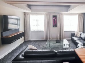A modern living room with a flat-screen TV, leather sofa, and a glass coffee table.