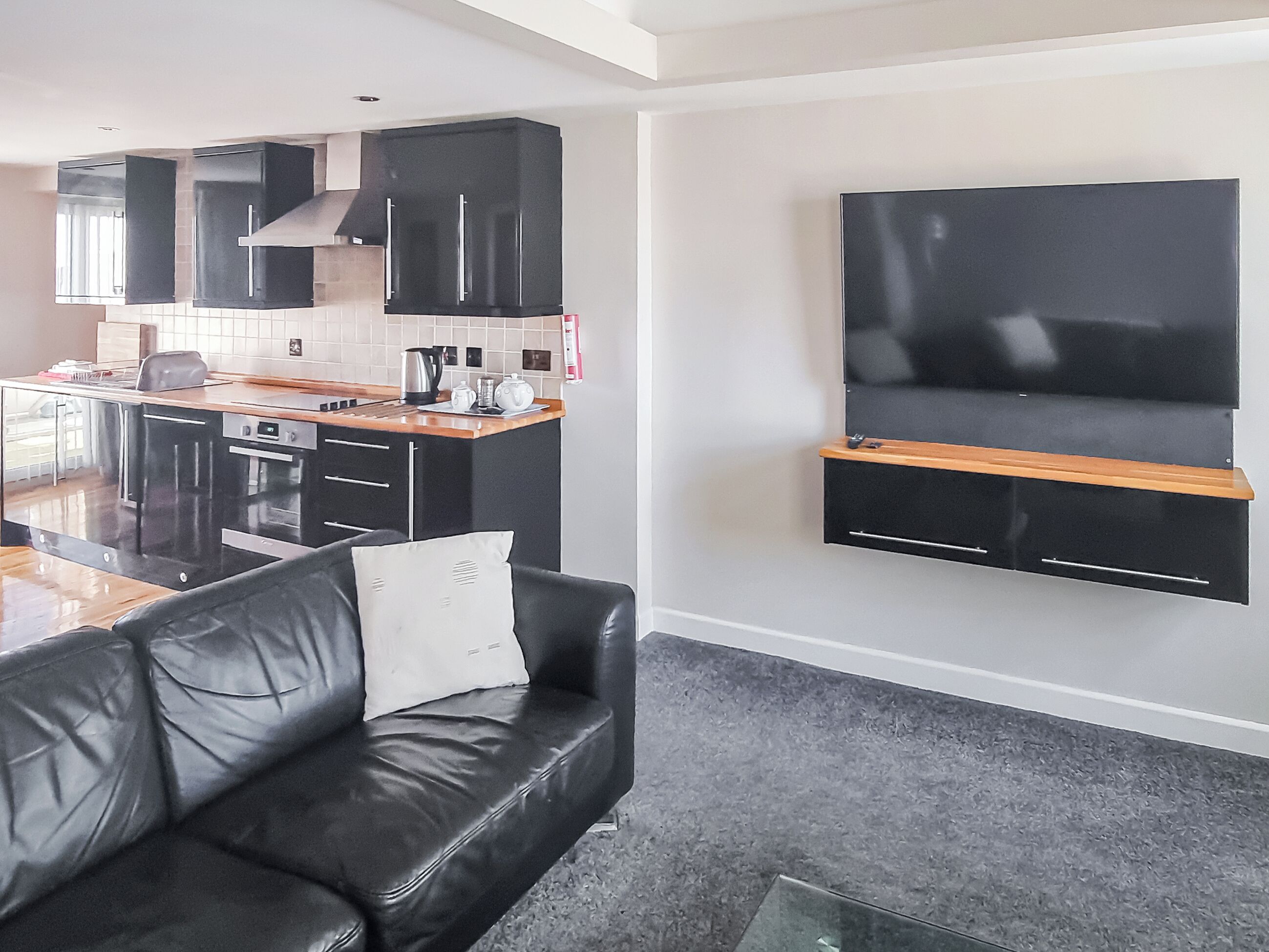 A modern kitchen with black cabinets, a wooden countertop, and a built-in TV.