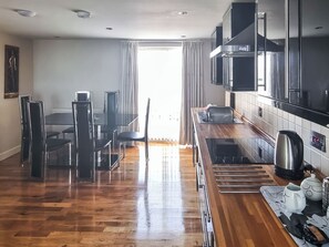 A modern kitchen with a dining area, wooden flooring, and a view of the outdoors.