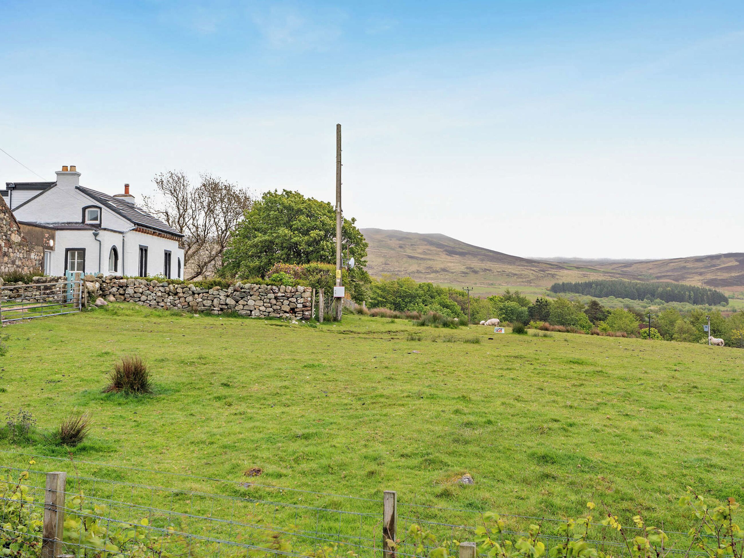 A rural landscape with a white house, stone wall, and a grassy field.