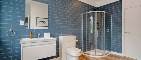 Une salle de bain avec des murs recouverts de carreaux bleus, un lavabo blanc, des toilettes, une douche en verre et un plancher en bois.