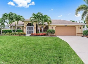 A residential house with a garage, a well-maintained lawn, and palm trees. - Spacious 4-bedroom house in charming Cape Coral neighborhood.   (Cape Coral)