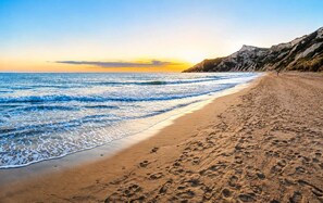 Ein Strand mit Wellen, blauem Himmel und einer felsigen Klippe.