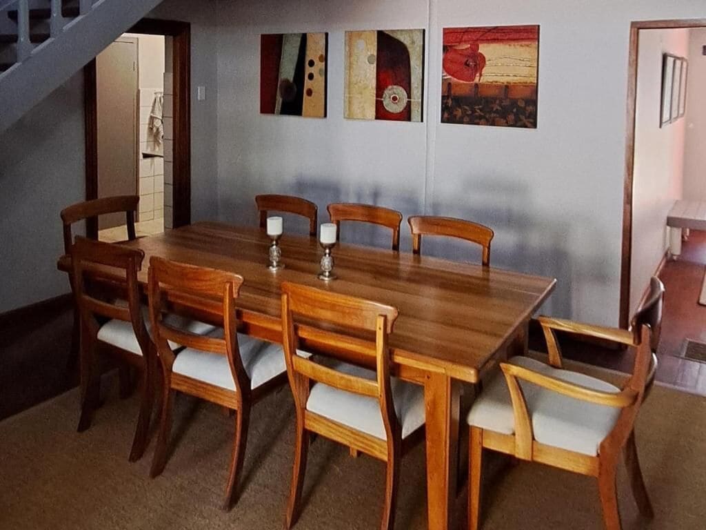A dining area with a wooden table and chairs, a staircase, and artwork on the wall.