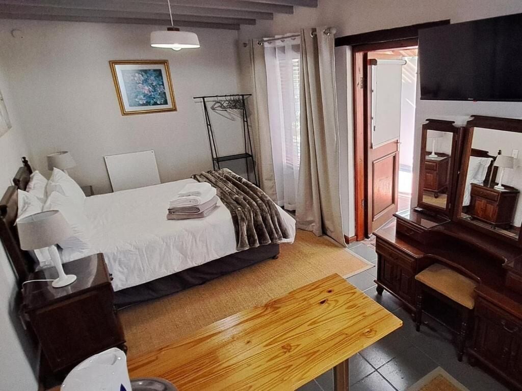 Ett hotellrum med en säng, ett nattduksbord, en lampa, en träbänk, en byrå, en spegel och en tavla på väggen.