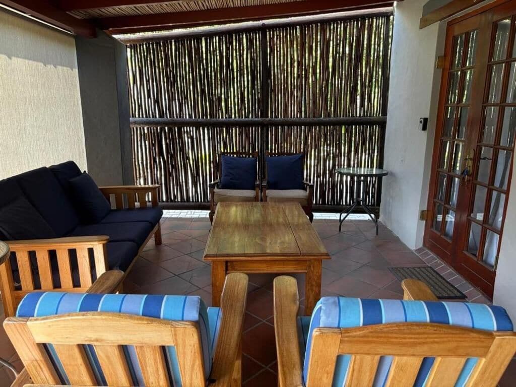 A covered patio area with wooden furniture, including a sofa and chairs, and a small table.