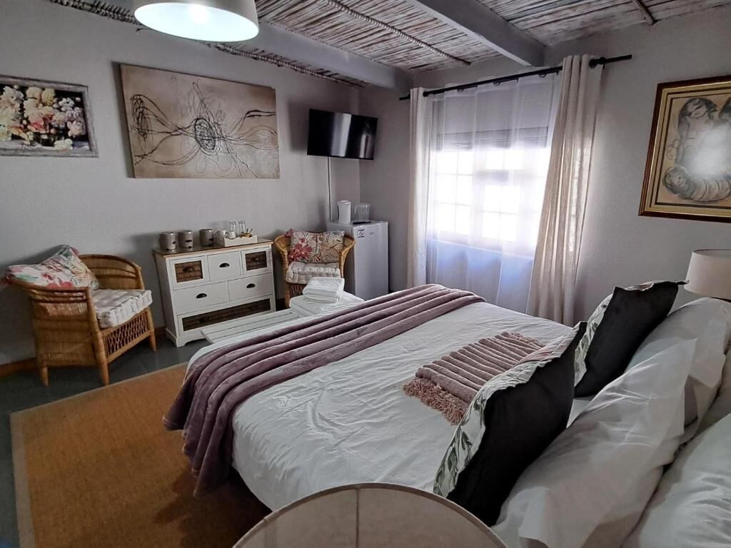 Une chambre à coucher comprenant un lit, une commode, une chaise, un téléviseur et une fenêtre avec des rideaux.