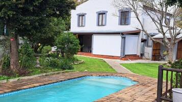 A residential property with a swimming pool, a covered patio, and a house with a sloped roof.
