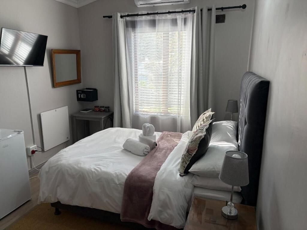 Een hotelkamer met een bed, een televisie, een nachtkastje met lamp en een raam met gordijnen.