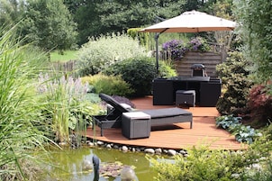 Una terraza con mobiliario exterior, una parrilla y un estanque.