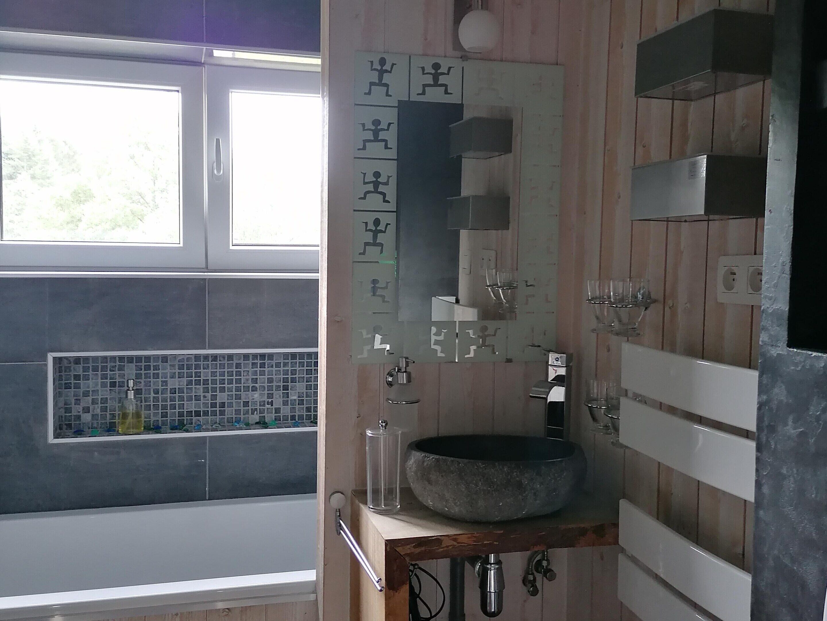 A bathroom with a large mirror, a stone sink, and a window with a view of trees.