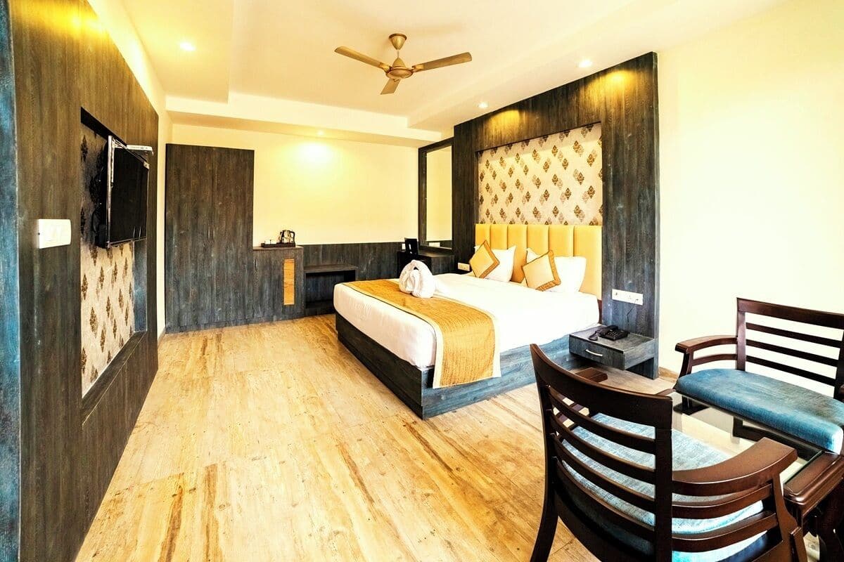 A hotel room with a bed, a desk, a chair, a TV, and a ceiling fan.