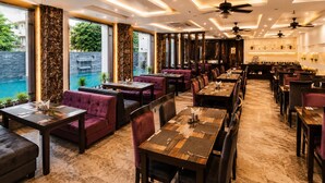 A restaurant with indoor seating, a pool view, and a modern interior design. - La Savanna Resort And Spa By DL Hotels And Resorts (Ramnagar)