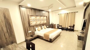 A hotel room with a bed, a desk, a chair, a television, and a ceiling fan. - La Savanna Resort And Spa By DL Hotels And Resorts (Ramnagar)