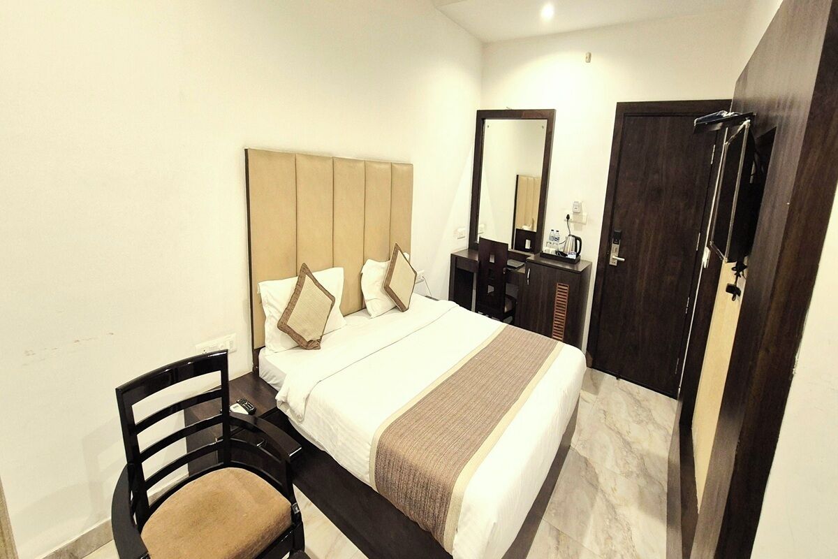 A hotel room with a bed, a desk, a chair, a dresser, a mirror, and a door.