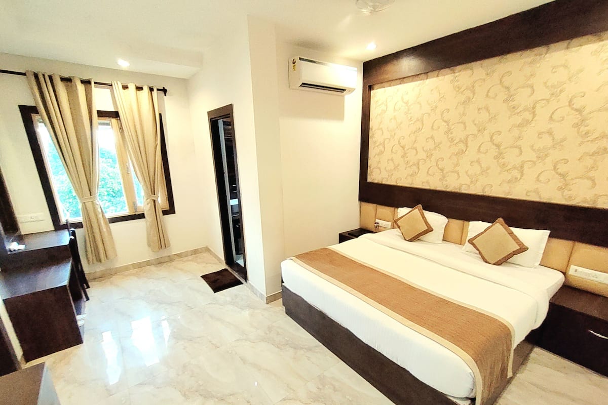 A hotel room with a bed, a desk, a chair, a wardrobe, and an air conditioning unit.
