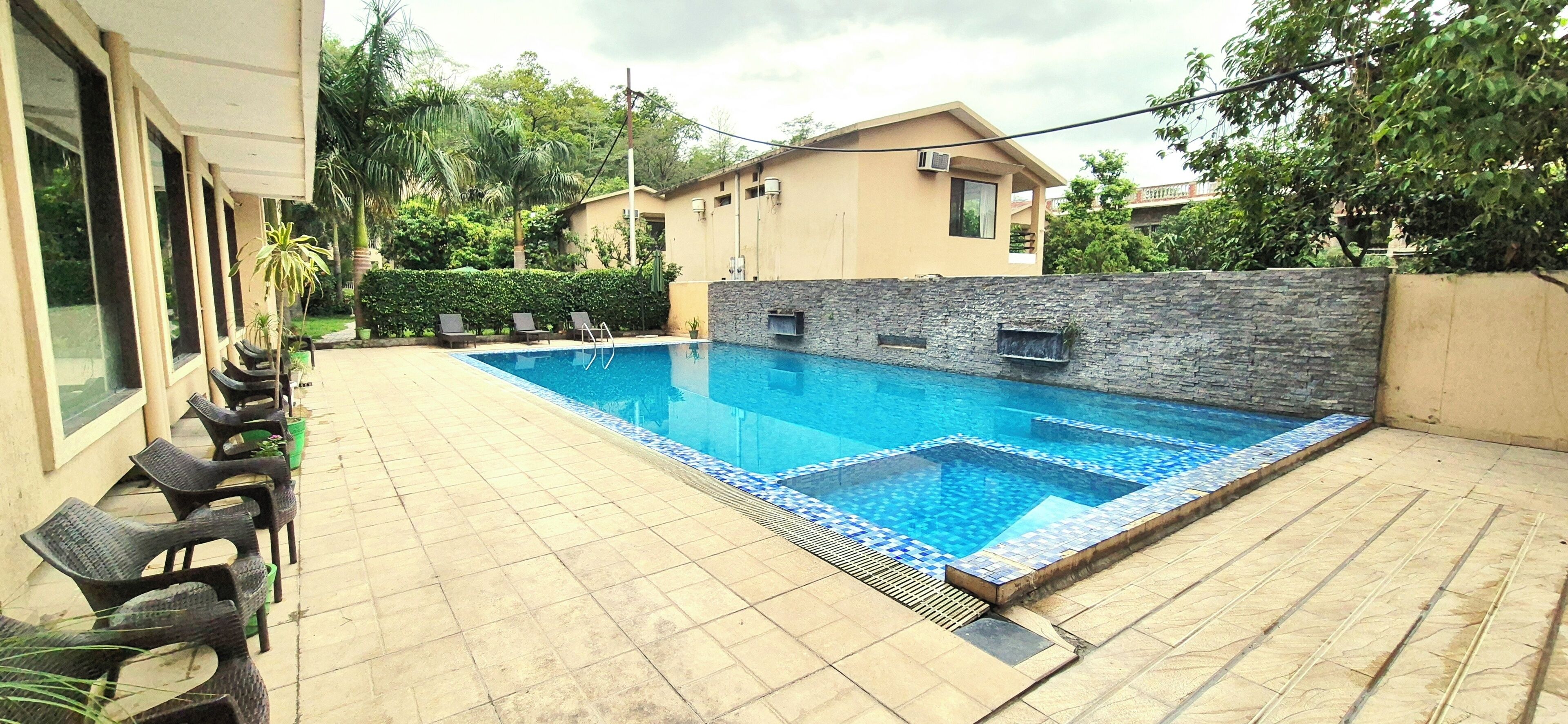 A swimming pool with a tiled edge, a stone wall, and a few lounge chairs.