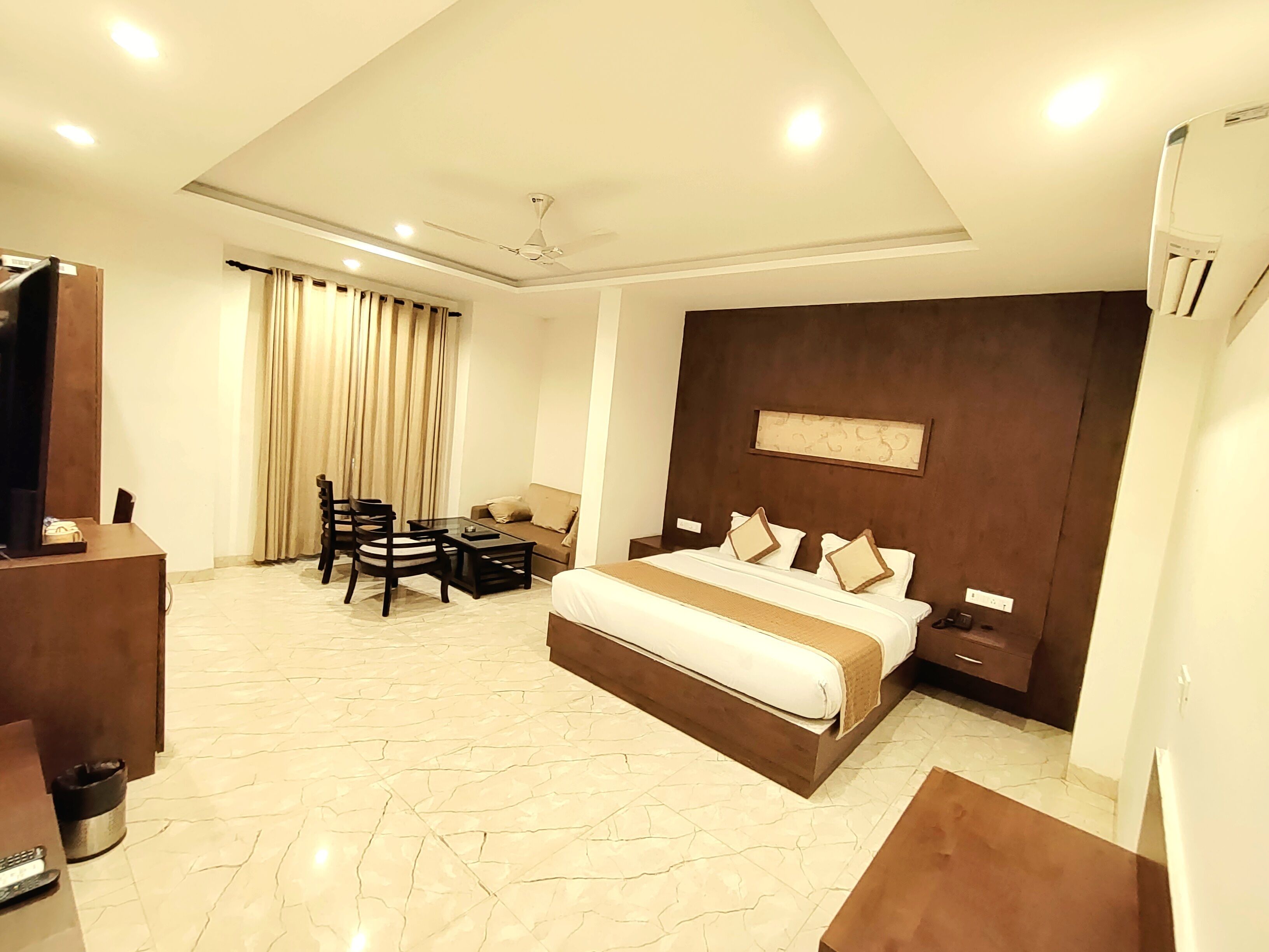 A hotel room with a bed, a desk, a chair, a table, a ceiling fan, and an air conditioning unit.