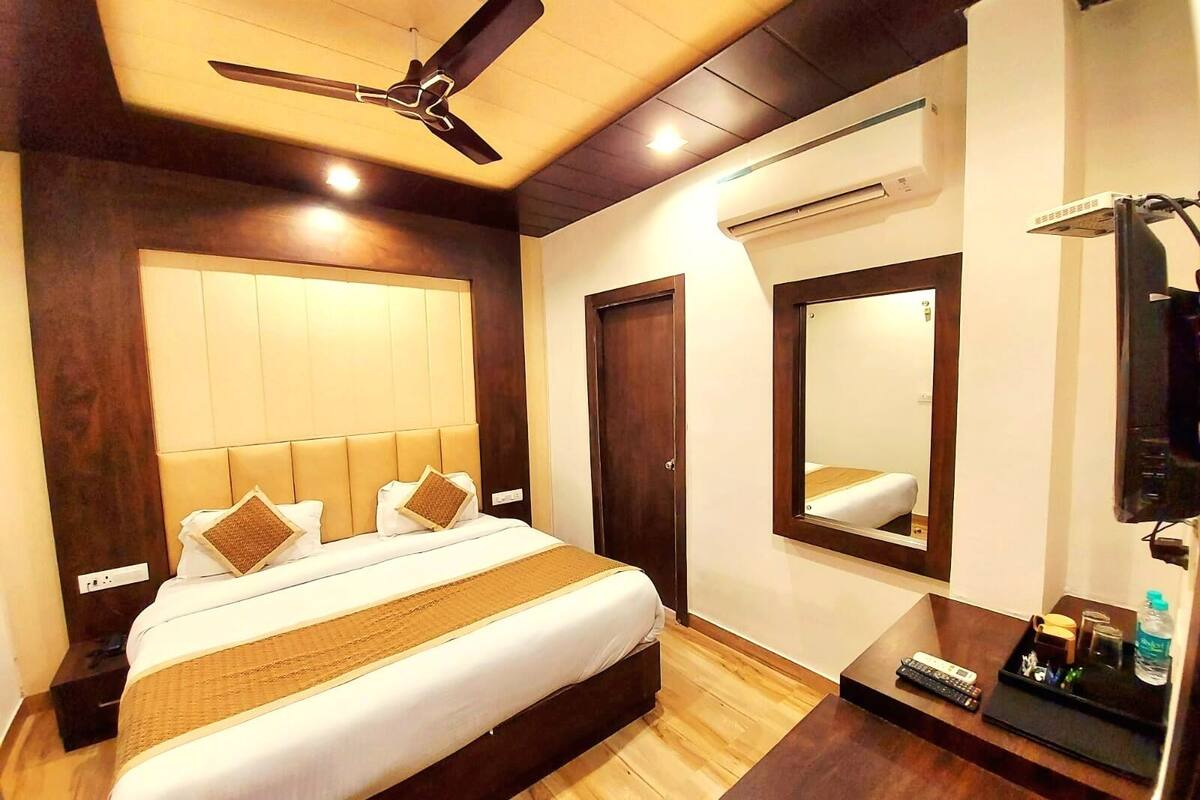 A hotel room with a bed, a ceiling fan, a mirror, a desk, and a TV.